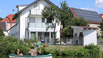 Una casa con balcón, panel solar y un río con un bote.