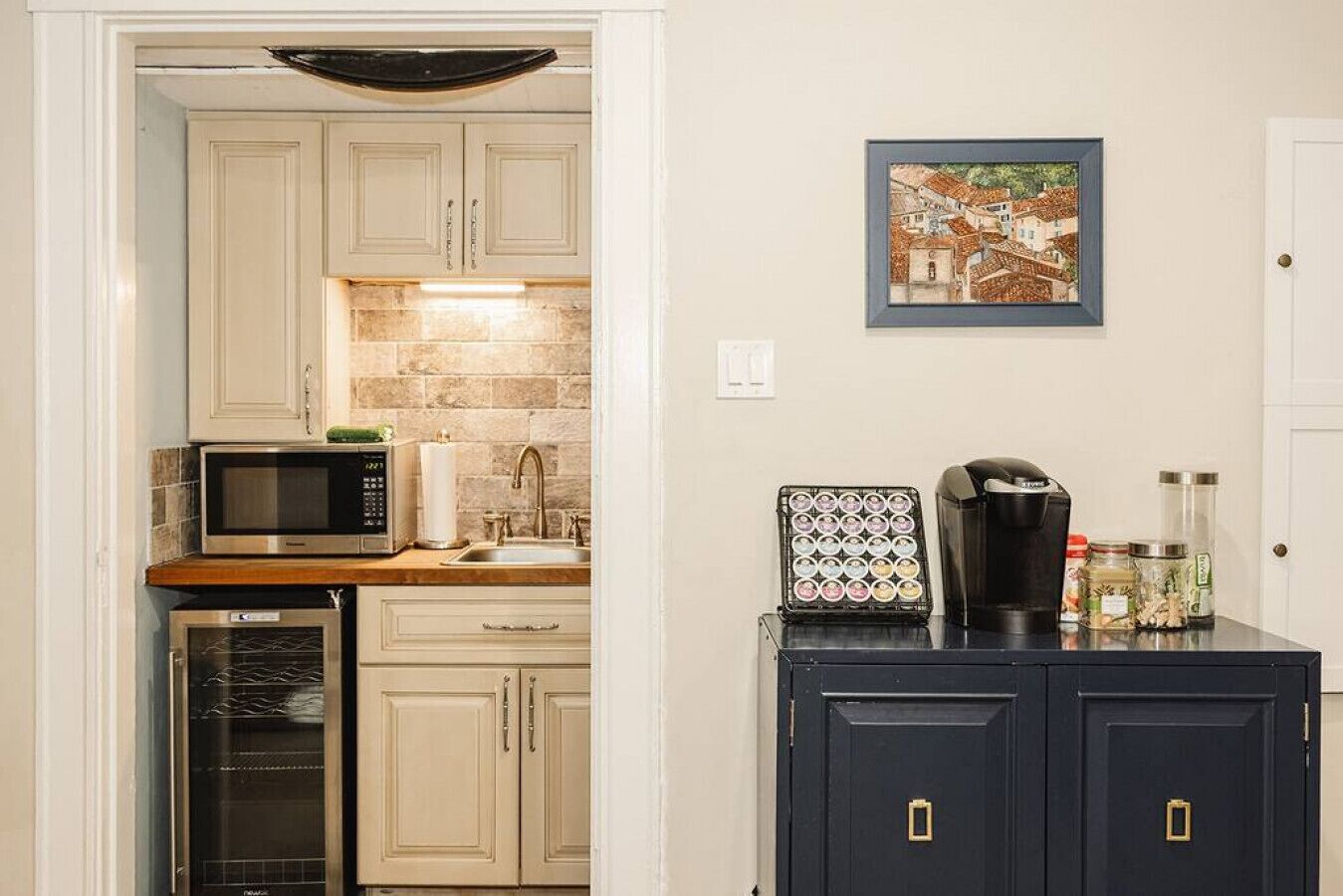 Una cocina con armarios blancos, microondas, cafetera y un cuadro en la pared.