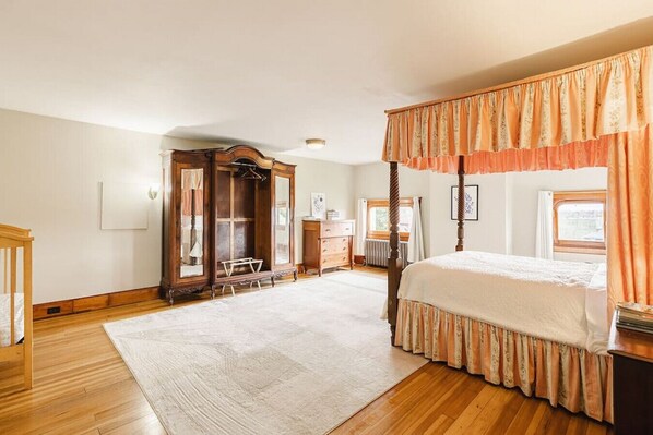 A bedroom with a four-poster bed, a wooden wardrobe, a dressing table, and a large window.