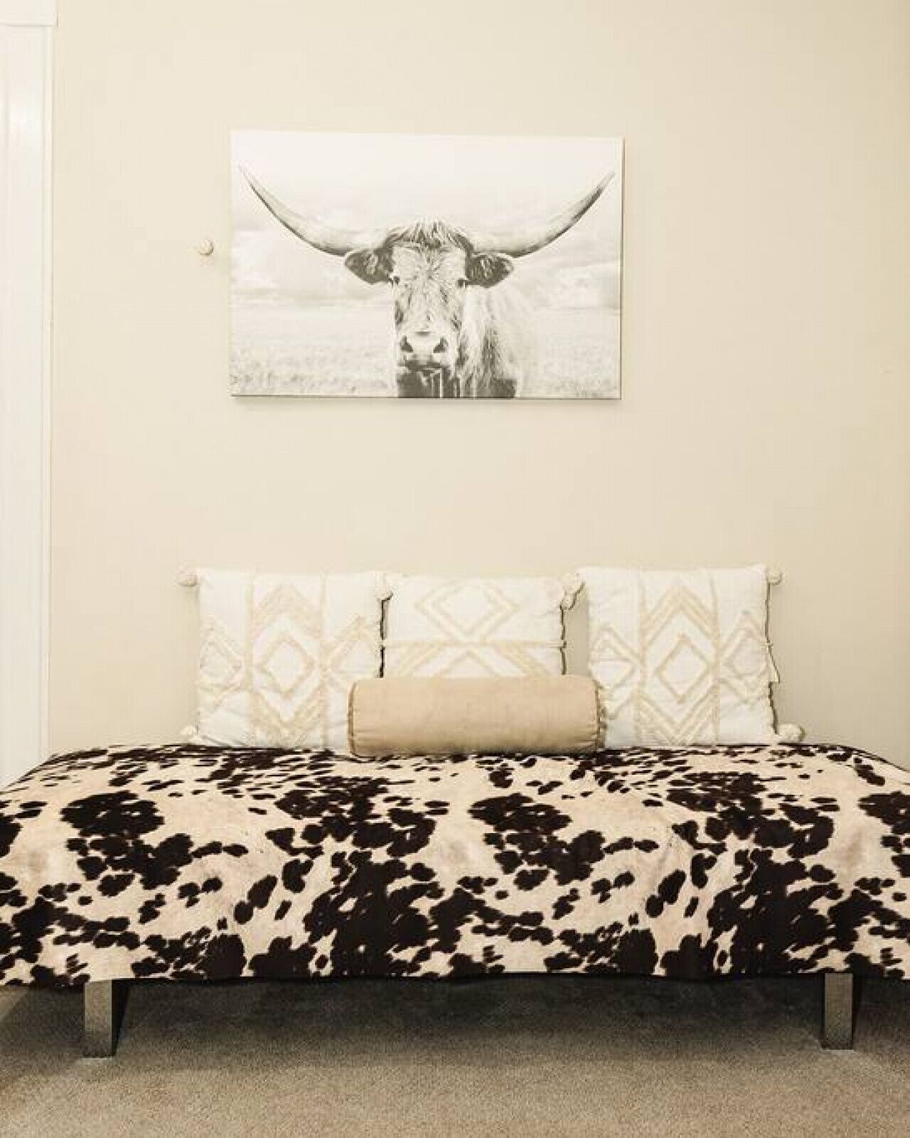 Un dormitorio con colcha de vaca, cabecero estampado y un adorno de vaca en la pared.