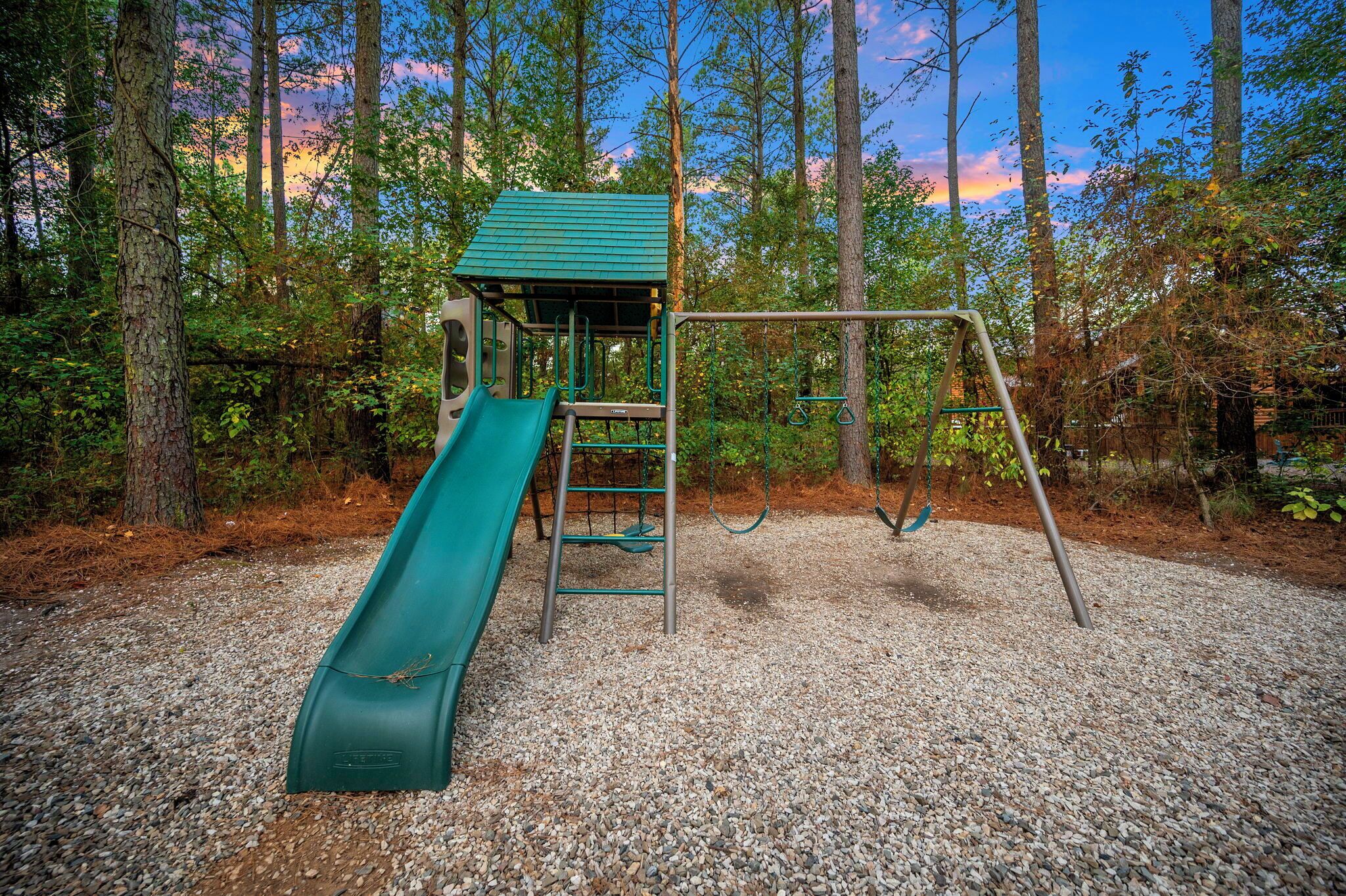 A playground with a slide, swings, and a climbing structure surrounded by trees.