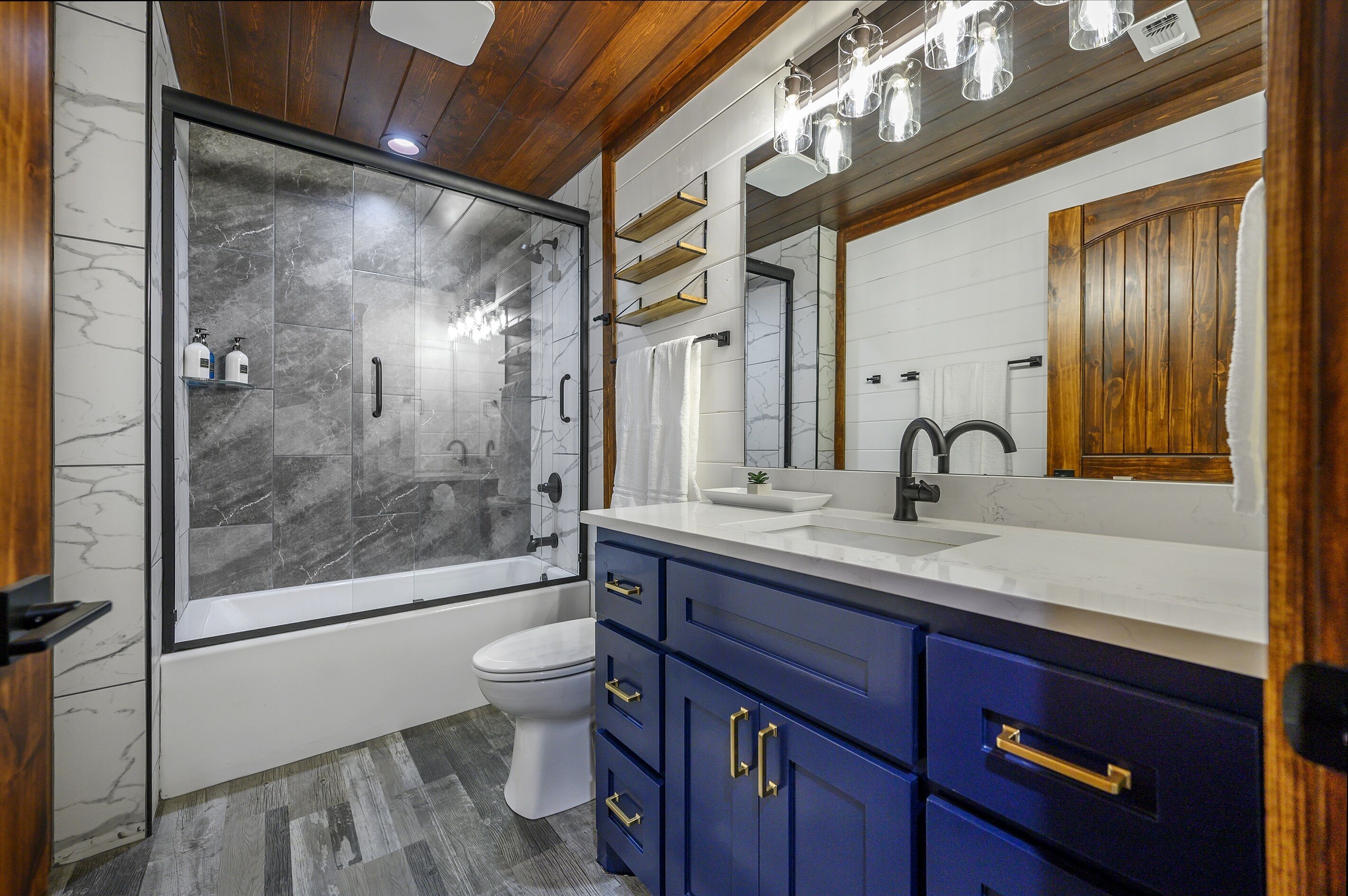 A modern bathroom with a glass-enclosed shower, a white toilet, and blue cabinets.