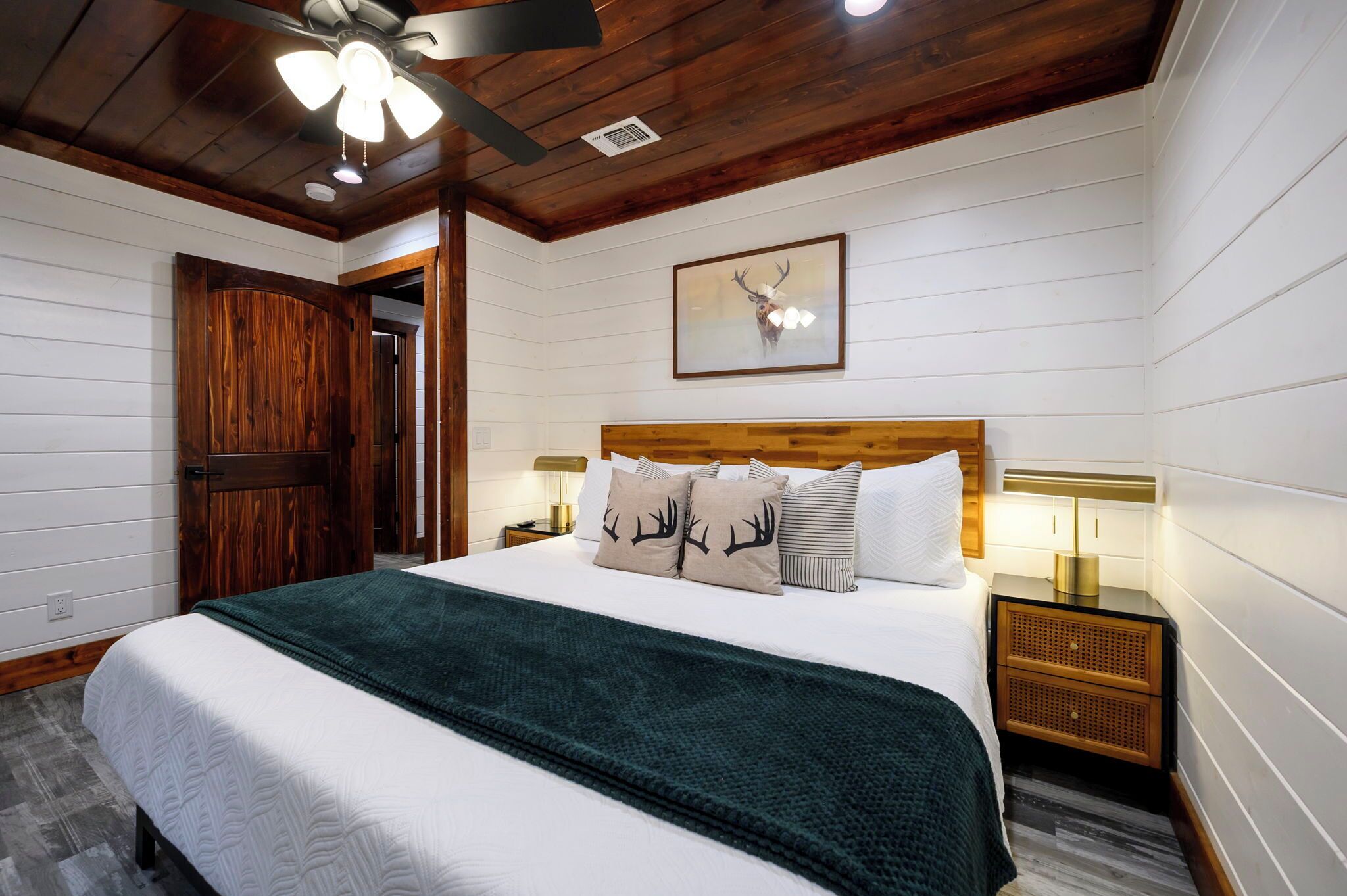 A bedroom with a wooden ceiling, a bed with white bedding, a green blanket, and a deer-themed pillow.
