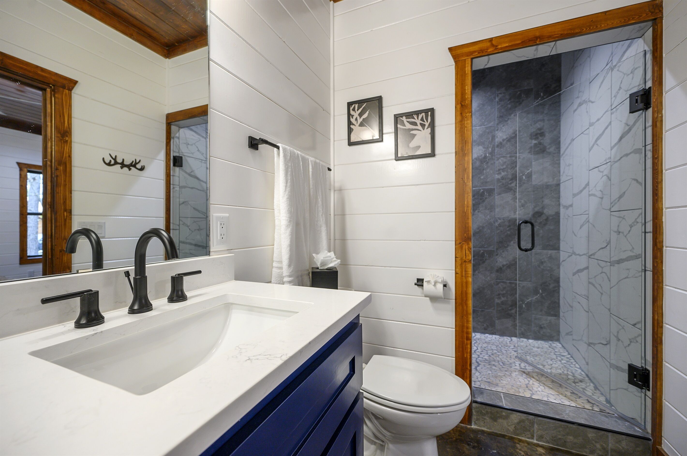 Un baño con un lavamanos blanco, grifos negros, un inodoro blanco y una cabina de ducha de vidrio.