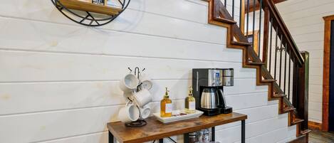 A wooden staircase with a coffee station featuring mugs, a coffee maker, and condiments.