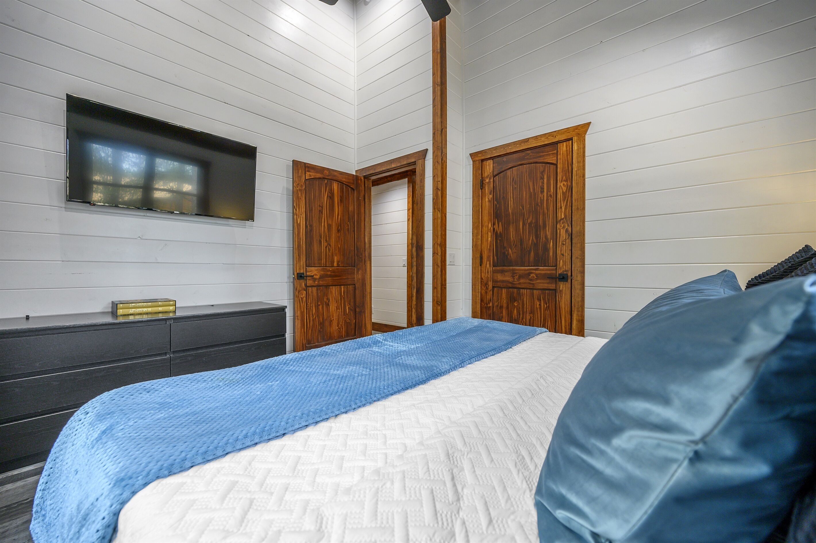 Een slaapkamer met een bed, een dressoir, een televisie en houten deuren.