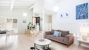 A modern living room with a sofa, coffee table, and dining area. - Mariners Retreat - by Latitude South Coast (Vincentia)