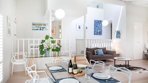 A modern living room with a glass dining table set for two, a brown sofa, and a white railing. - Mariners Retreat - by Latitude South Coast (Vincentia)