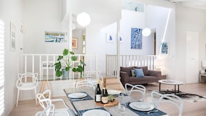 A modern living room with a glass dining table set for two, a brown sofa, and a white railing.