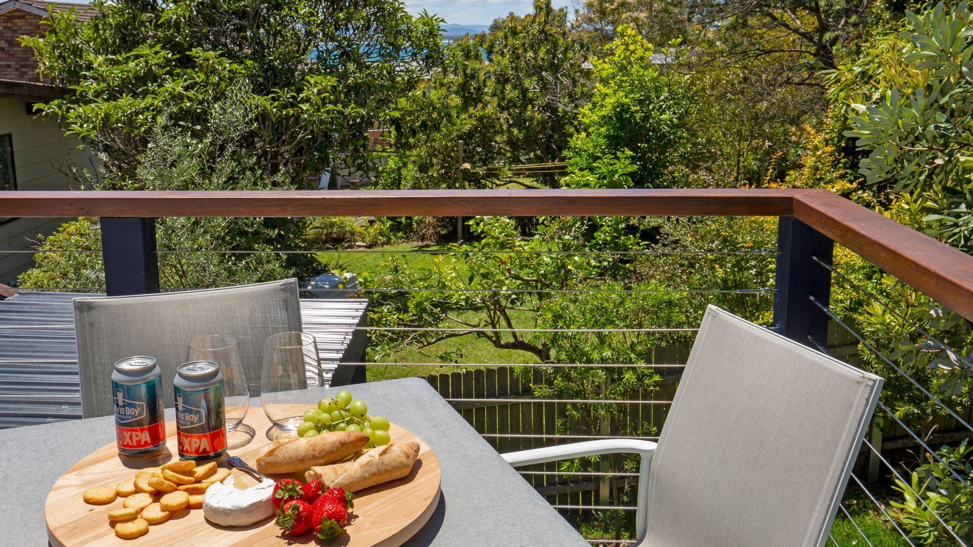 A balcony with a table set for a meal, including snacks, drinks, and a fruit platter.