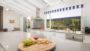 A modern kitchen with a large island, stainless steel appliances, and a view of greenery outside. - Mariners Retreat - by Latitude South Coast (Vincentia)