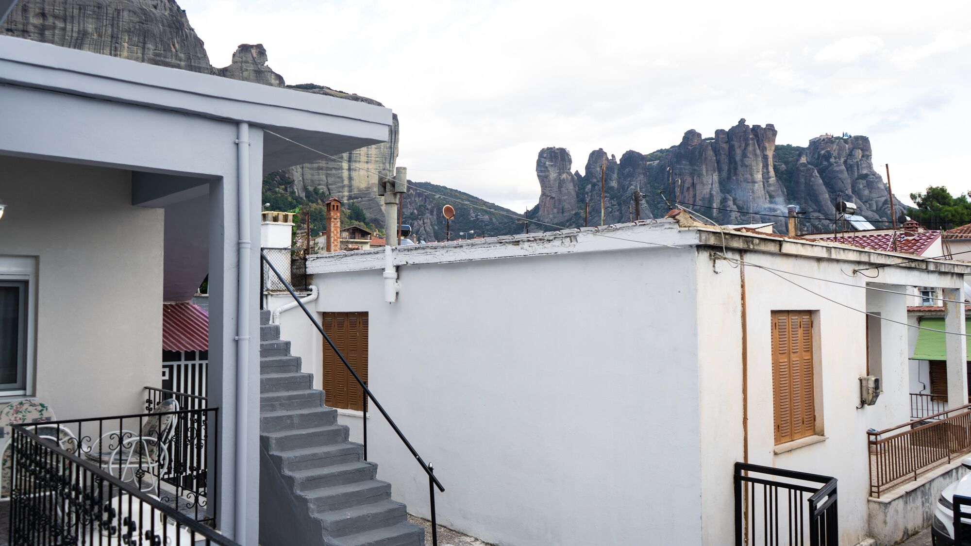 Edificio residencial con una escalera que lleva a un balcón, fachada blanca y vistas a acantilados rocosos al fondo.