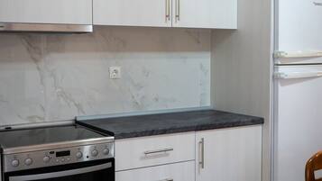 A kitchen with white cabinets, a black countertop, a built-in oven, and a refrigerator.