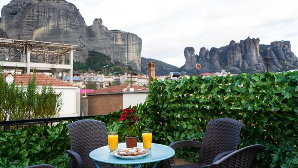 A terrace with two wicker chairs, a small table, a potted plant, and a plate of food with two glasses of orange juice. - Andromachis Moneto Under Meteora (Kalabaka)