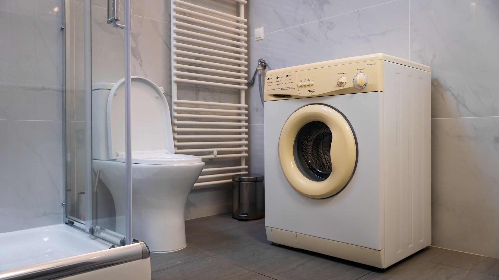 Une salle de bain moderne avec une douche à parois de verre, des toilettes, un lave-linge et un radiateur.