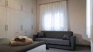 A bedroom with a bed, a grey sofa, a wardrobe, and a window with curtains. - Andromachis Moneto Under Meteora (Kalabaka)