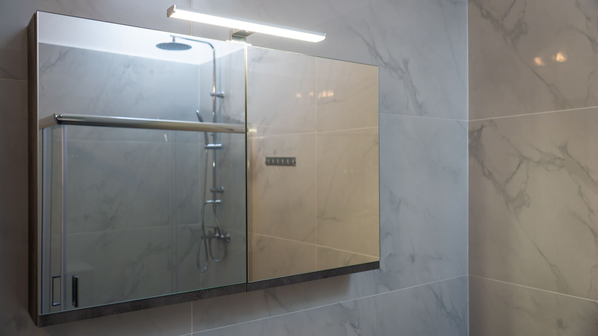 Une salle de bain moderne dotée d’une douche à parois de verre, de carreaux de marbre et d’un panneau de commande visible.