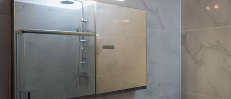 Une salle de bain moderne dotée d’une douche à parois de verre, de carreaux de marbre et d’un panneau de commande visible.