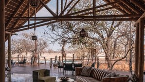 Eine Lounge im Freien mit hoher Holzkονstruktion, Sitzgelegenheiten und Blick auf die umliegende Landschaft.