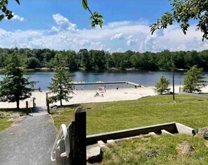 Un parc au bord du lac, doté d’une plage de sable, d’une terrasse en bois et d’une pelouse.