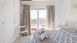 Habitación de hotel con cama, una silla, ventana con cortinas, equipo de aire acondicionado y vistas a un edificio.