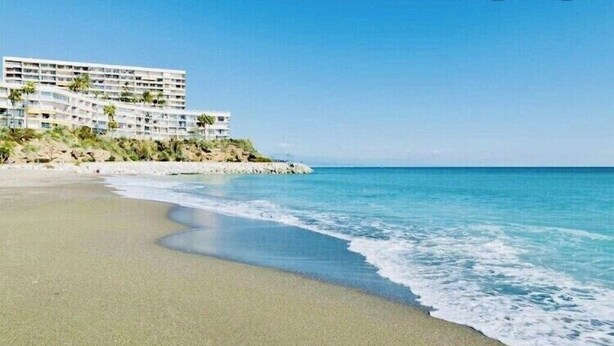 Un hotel frente a la playa con varios pisos, una playa de arena y olas del océano.