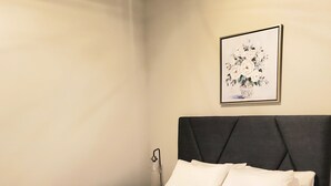 A neatly made bed with white linens in a room with a dark headboard and a framed floral painting on the wall. - Newly Renovated "Arctic Rose" Loft in Historic Florence (Florence)