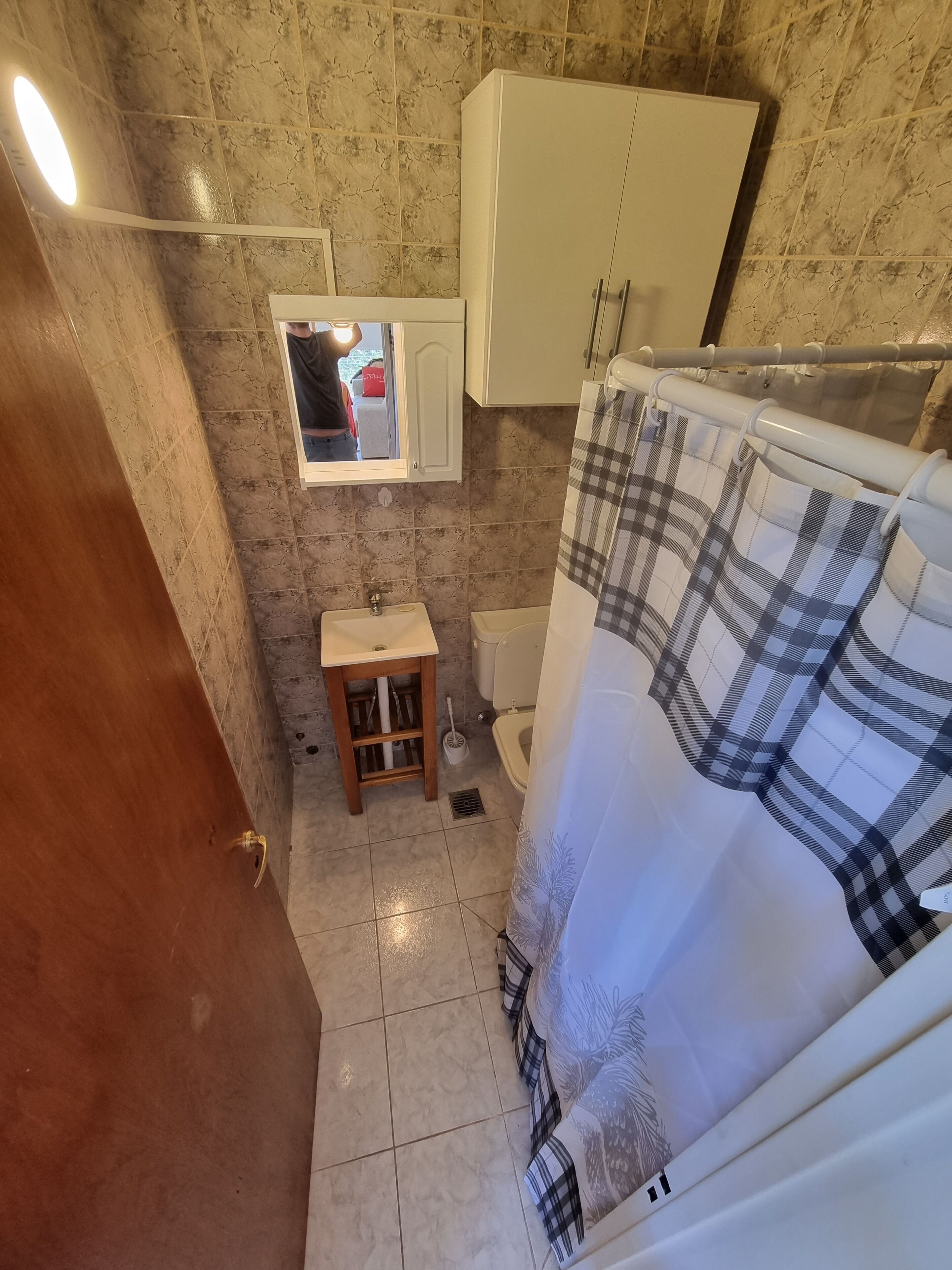 A bathroom with a toilet, sink, and a mirror above the sink. There is a shower curtain with a plaid pattern.