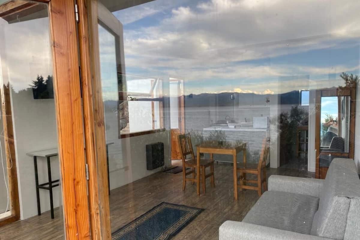 A spacious balcony with a view of the water, wooden flooring, a grey sofa, and a small table with chairs.