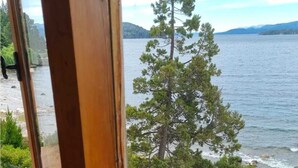 Ett träfönster med utsikt över en sjö, träd och ett bergskedja i fjärran.