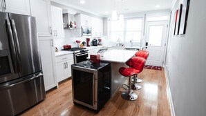 A modern kitchen with white cabinets, stainless steel appliances, and a central island with red bar stools. - Modern Smart Home w/Gourmet Kitchen, Peloton & King Suite  with Rooftop Deck (Baltimore)