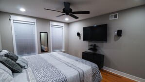 A bedroom with a bed, ceiling fan, TV, and a small cabinet. - Modern Smart Home w/Gourmet Kitchen, Peloton & King Suite  with Rooftop Deck (Baltimore)
