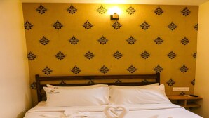Una cama impecablemente hecha con una toalla dispuesta en forma de cisne, un cabecero de madera y una pared con papel tapiz estampado.