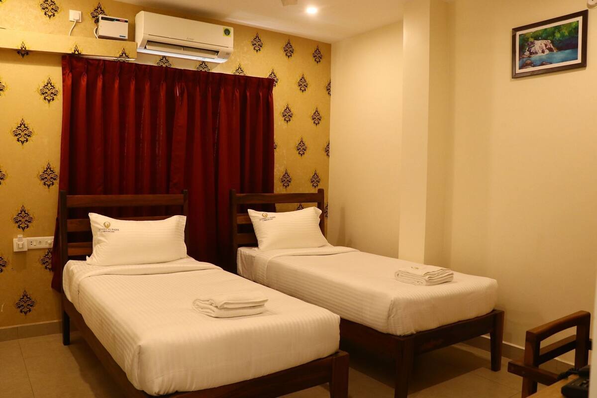 Habitación de hotel con dos camas individuales, una cortina roja, un equipo de aire acondicionado y un cuadro en la pared.