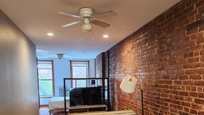 A modern living space with a brick wall, a ceiling fan, and a dining area with a table and chairs. - Studio boutique à 2 min do Central Park (New York)