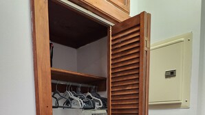 A small walk-in closet with wooden doors, a metal rack with hangers, and a beige electrical box on the wall. - Studio boutique à 2 min do Central Park (New York)