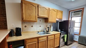 A kitchen with wooden cabinets, a stainless steel sink, a stove, and a refrigerator. - Studio boutique à 2 min do Central Park (New York)