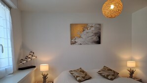 Ein Schlafzimmer mit einem großen Bett, zwei Nachttischen mit Lampen, einem Fenster mit Vorhängen, einem Wandbild und einer Pendelleuchte.