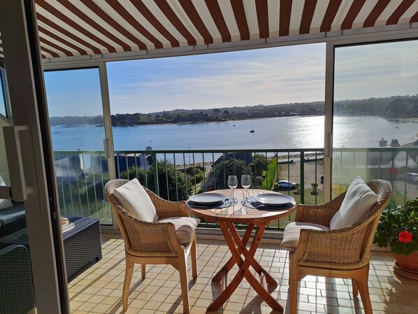 A balcony with wicker chairs, a table set for two, and a view of a body of water. - Trégastel, Pink Granite Coast - Apartment SEA ANEMONE***with panoramic sea view (Trégastel)