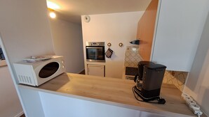 Eine kleine Küche mit einer Mikrowelle, einem Backofen und einer Kaffeemaschine auf der Arbeitsfläche.