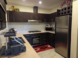 A modern kitchen with dark cabinets, a stainless steel refrigerator, a microwave, and a gas stove.