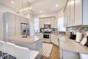 A modern kitchen with white cabinetry, a central island, stainless steel appliances, and a patterned rug.