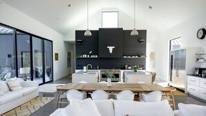 Eine moderne Küche mit Kochinsel, ein Essbereich mit Holztisch und ein Wohnzimmer mit weißem Sofa.