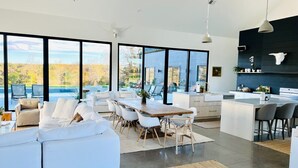 Ein moderner, offener Wohn- und Essbereich mit großen Fenstern, einer Küche und einer Sitzecke mit weißem Sofa und Esstisch.
