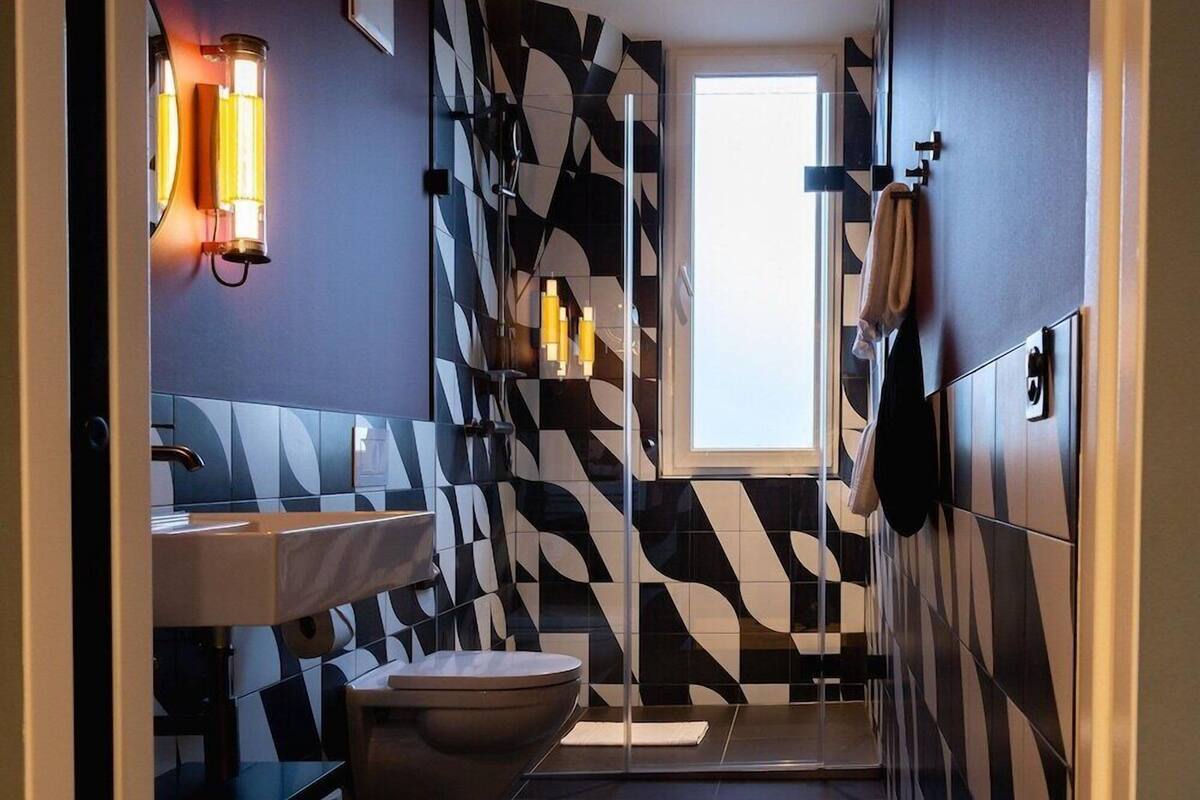 Un baño moderno con un diseño de baldosas geométricas, un lavamanos blanco, un inodoro y una zona de ducha.