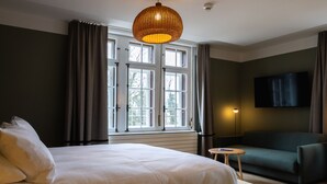 Una habitación de hotel con una cama grande, un sofá, un televisor y una ventana con cortinas.