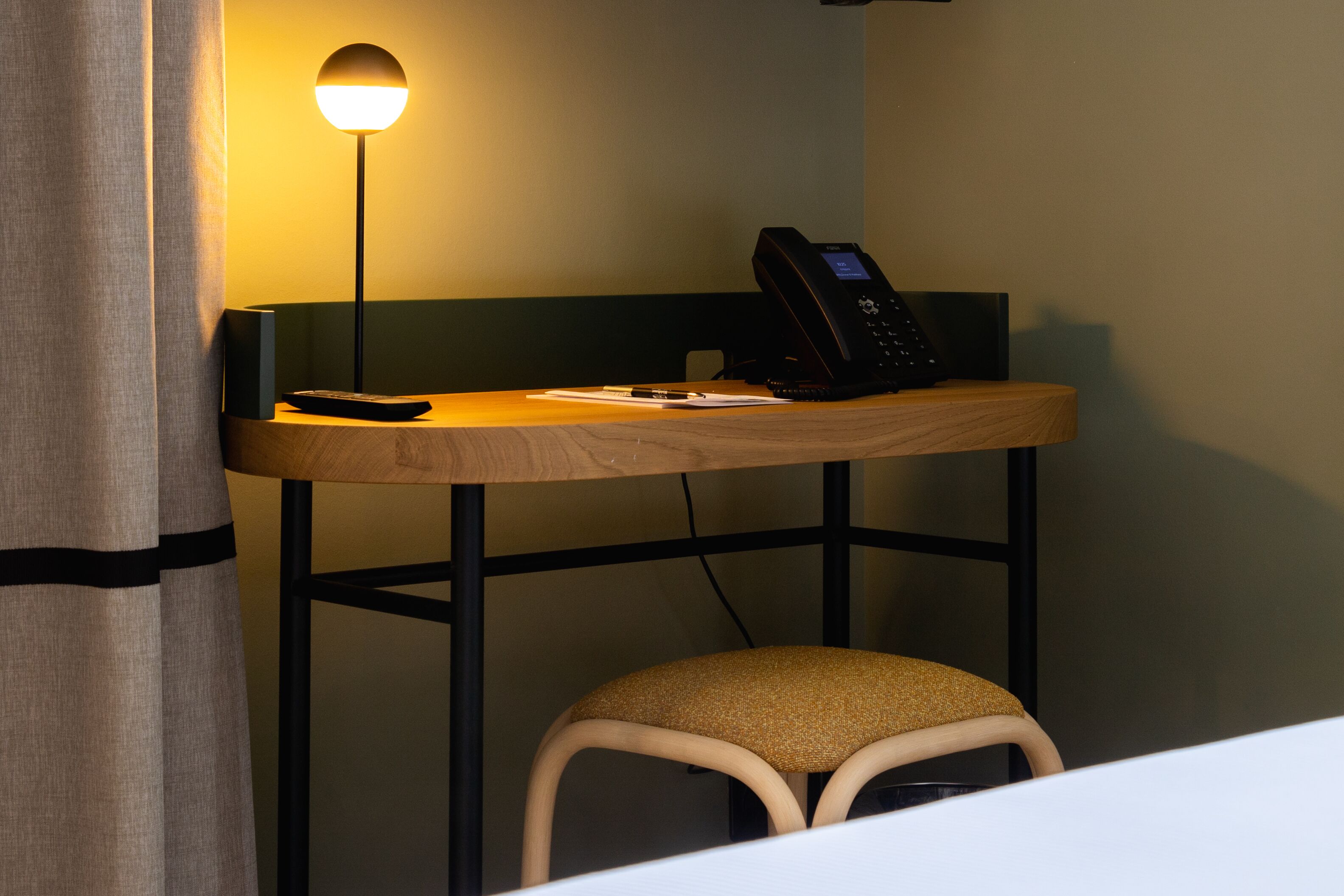 A small wooden desk with a telephone, a remote control, and a smartphone.
