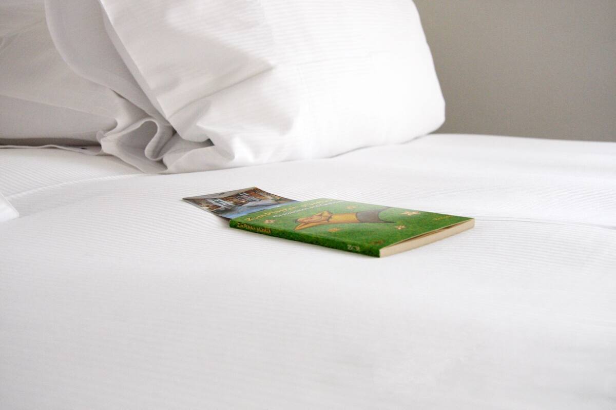 Un libro titulado "Zum ersten Mal" sobre una cama blanca con un almohadón.