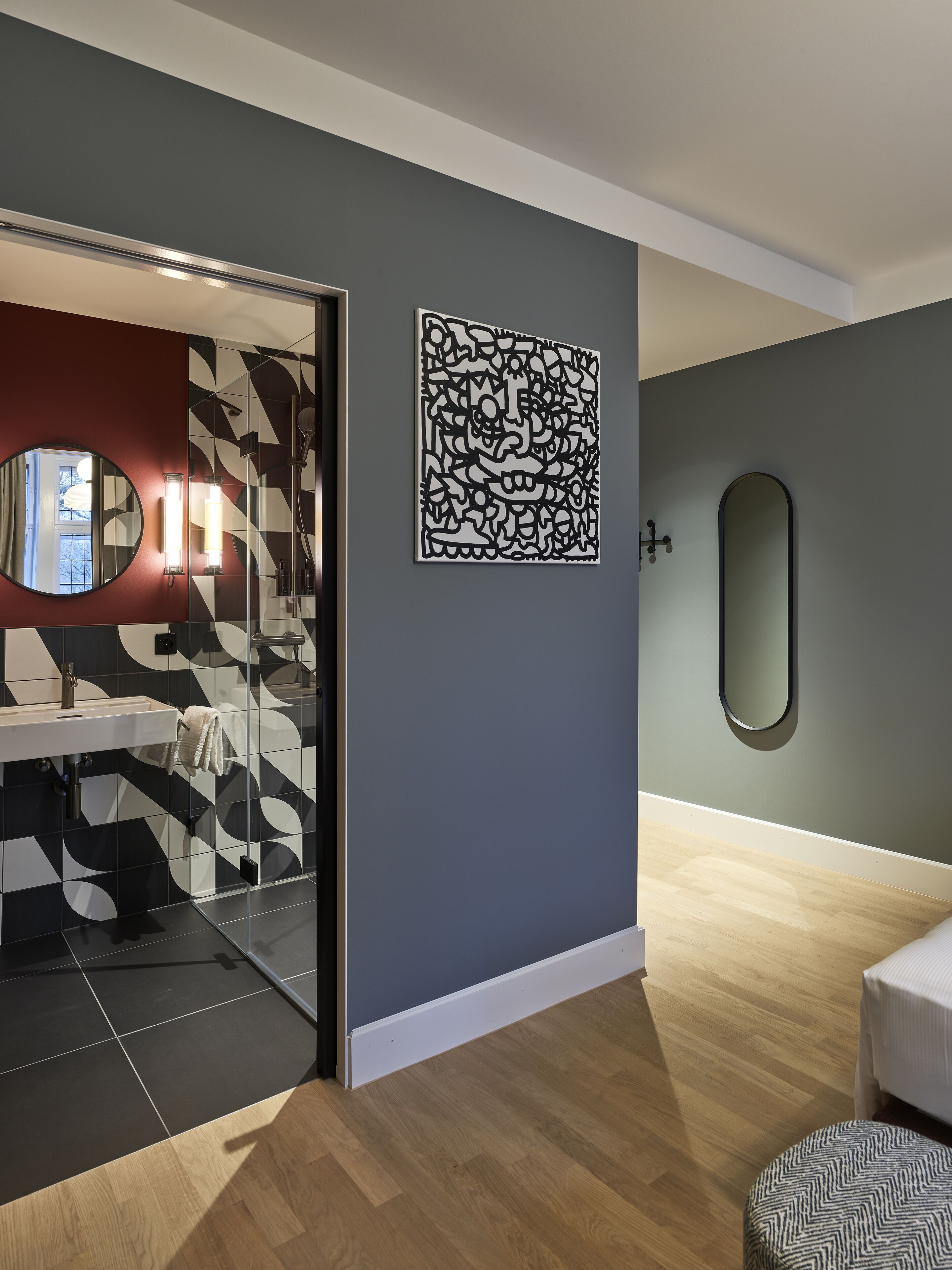 Un baño moderno con cabina de ducha de vidrio, un espejo redondo y una obra de arte geométrico en la pared.