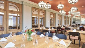 Un restaurante espacioso con techos altos, ventanas amplias y varias mesas dispuestas para los comensales.